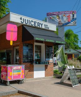 Exterior of The Juicery’s Kittery location with walk-up ordering window, menu boards, and colorful signage.