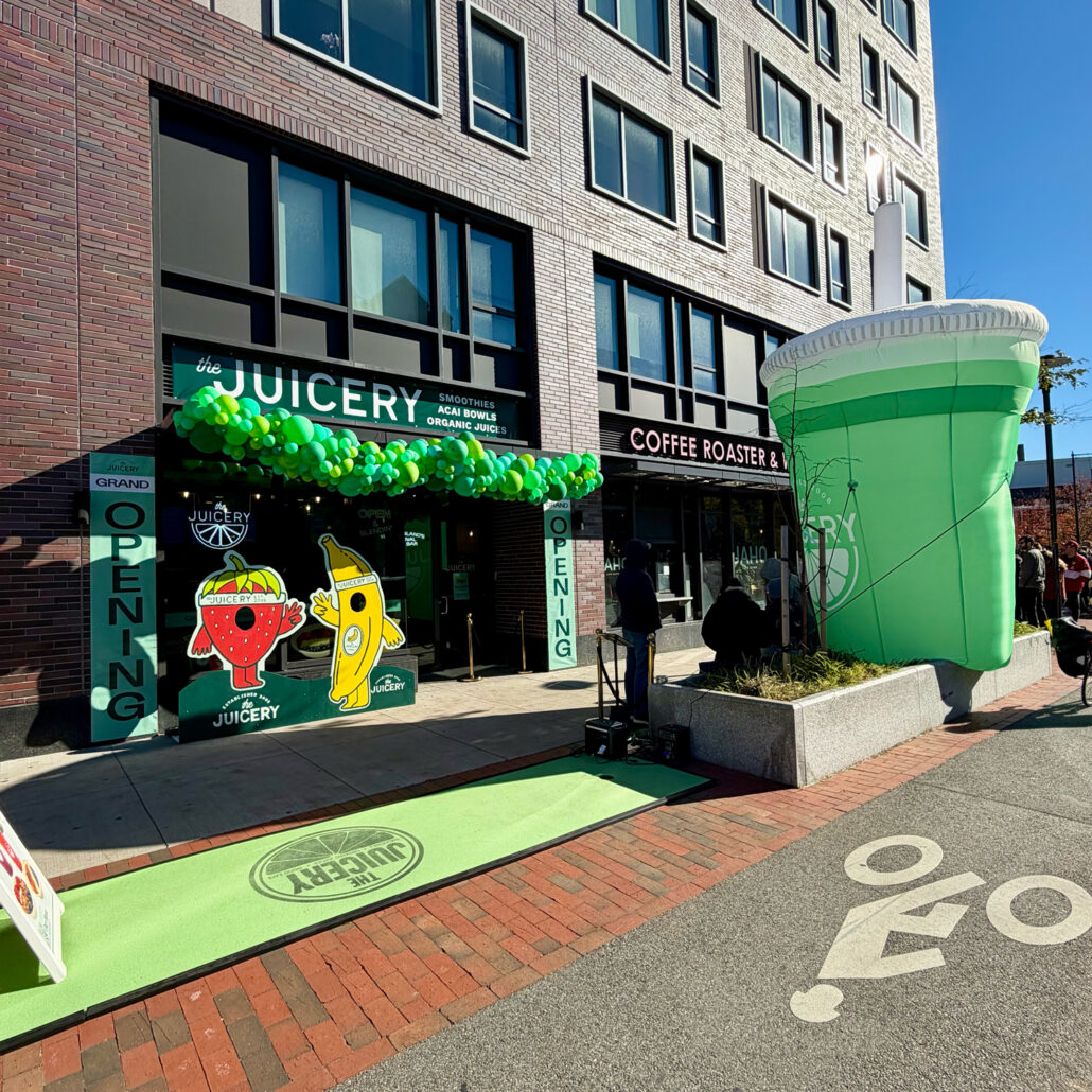 Exterior of The Juicery’s Cambridge location decorated with green balloons and window graphics during the grand opening.