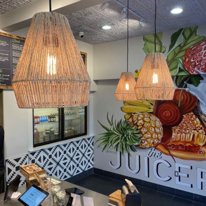Interior of The Juicery’s Boston University location with pendant lighting, counter seating, and a fruit-inspired wall mural.